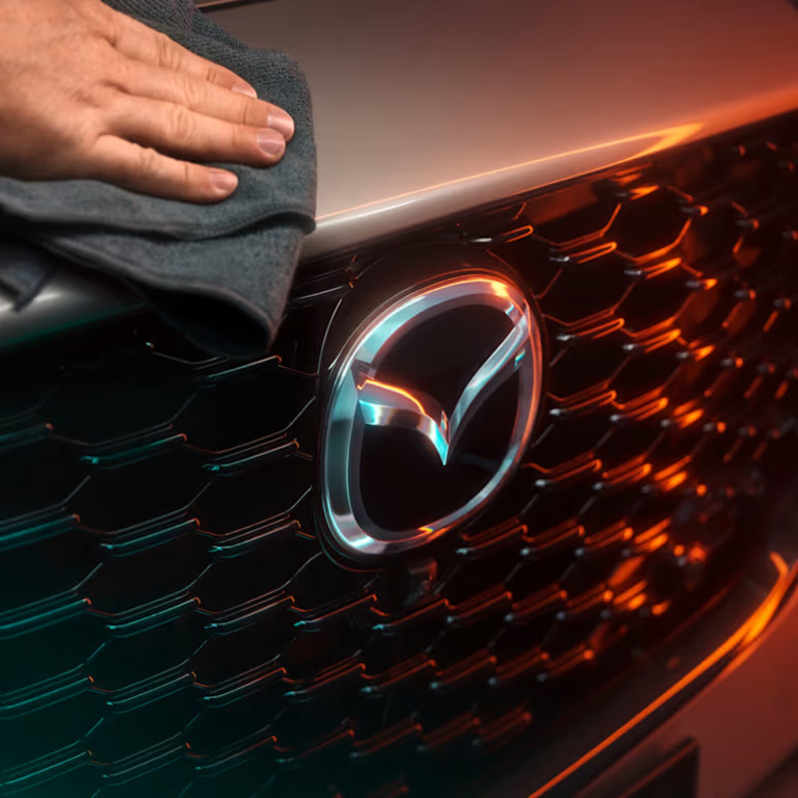 Eine Hand poliert den Kühlergrill eines Mazda mit einem Tuch